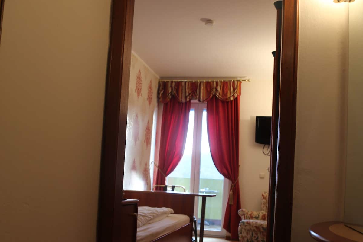 A narrow hallway leading to a bedroom with a bed, a small table, and a chair.