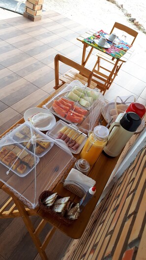 A breakfast buffet with various food items and beverages on a wooden table. - Chalés Barra do Sol (Cajueiro da Praia)