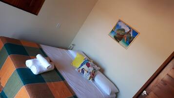 A single bed with a checkered blanket, a floral pillow, and rolled towels on the side.