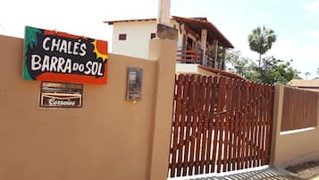 A sign for 'Chales Barra do Sol' with a wooden fence and a small building with a tiled roof.
