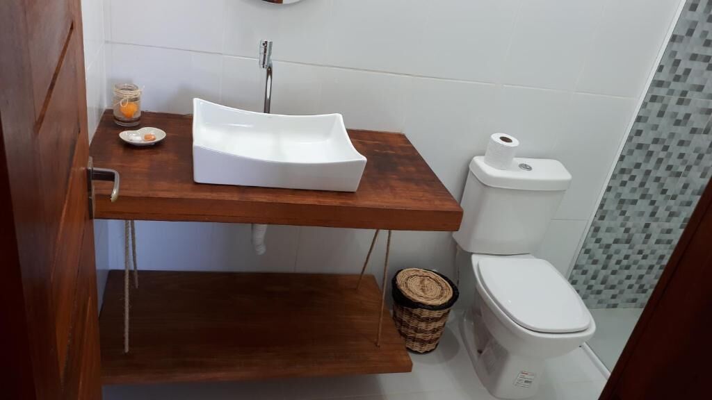 A bathroom with a wooden vanity, a white sink, a toilet, and a small trash bin.