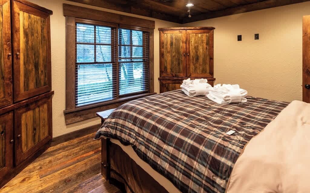 A bedroom with a wooden floor, a bed with a plaid bedspread, and wooden wardrobes.