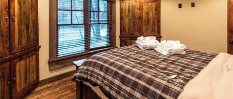 A bedroom with a wooden floor, a bed with a plaid bedspread, and wooden wardrobes.