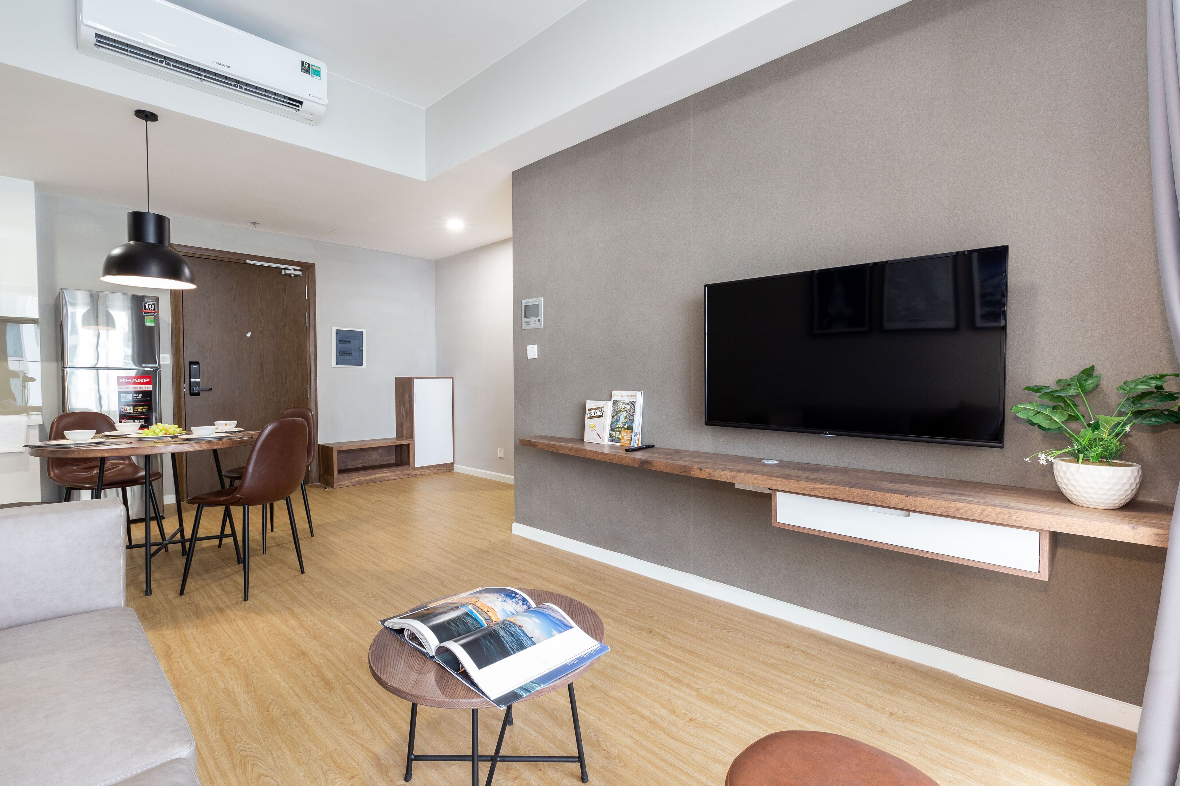 Ein modernes Wohnzimmer mit Flachbildfernseher, Holzboden, einem Essbereich mit Stühlen, einem Sofa und einer Zeitschrift auf einem kleinen Tisch.