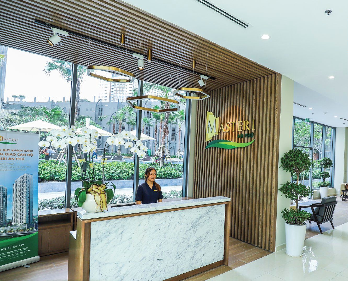 A modern hotel reception area with a wooden reception desk, a receptionist, and a view of the cityscape through large windows.