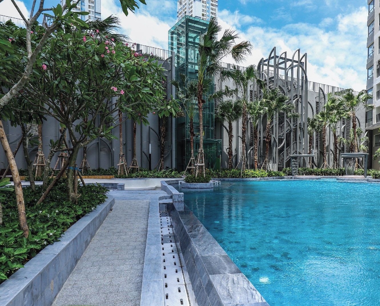 A modern hotel with a large ocean pool surrounded by lush greenery and tall buildings.