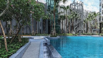 A modern hotel with a large ocean pool surrounded by lush greenery and tall buildings.