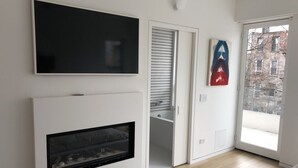Een moderne kamer met een flatscreen televisie boven een open haard, een schuifdeur naar een balkon en een kunstwerk in een lijst aan de muur.