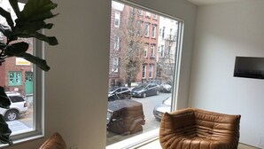 Een moderne woonkamer met leren banken, een groot raam met uitzicht op een stadsstraat en een wandtelevisie.