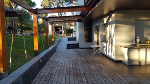 A covered outdoor deck with a wooden floor, a small round table, and a grill area. - Spectacular villa with private pool and large spaces  (Caldes de Montbui)