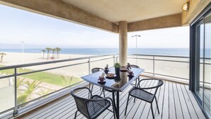 Ein Balkon mit Tisch und Stühlen mit Blick auf einen Strand mit Palmen und dem Meer.