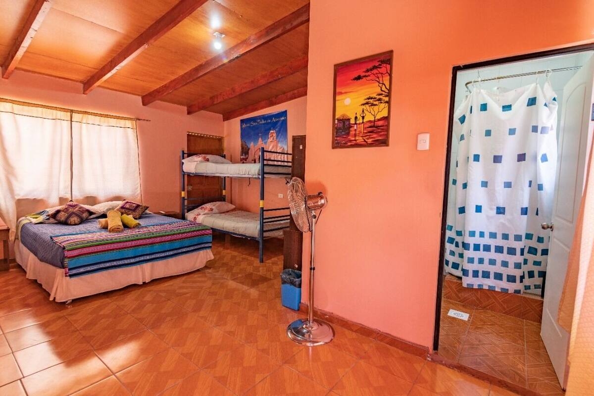 Ein Zimmer mit einem Etagenbett, einem Standventilator, einem Poster an der Wand und einer Duschvorhang.