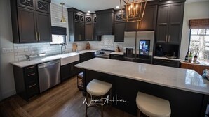 A modern kitchen with dark cabinetry, a large island, stainless steel appliances, and a pendant light fixture. - Discover Your Perfect Getaway: Cottage in the Heart of Horse & Bourbon Country! (Midway)