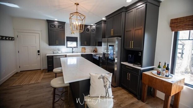 A modern kitchen with dark cabinetry, a large island, and a wooden bar stool. - Discover Your Perfect Getaway: Cottage in the Heart of Horse & Bourbon Country! (Midway)