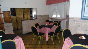 A dining area with tables set for four, each with a pink tablecloth and black chairs. There is a kitchen area with a wooden counter and a refrigerator. - Hotel San Francisco (San Juan)