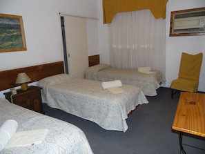 A hotel room with three beds, a wooden nightstand with a lamp, a chair, and a table. - Hotel San Francisco (San Juan)