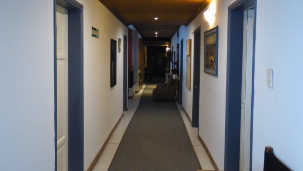 A hotel hallway with doors on both sides, a carpeted floor, and a bench at the end. - Hotel San Francisco (San Juan)