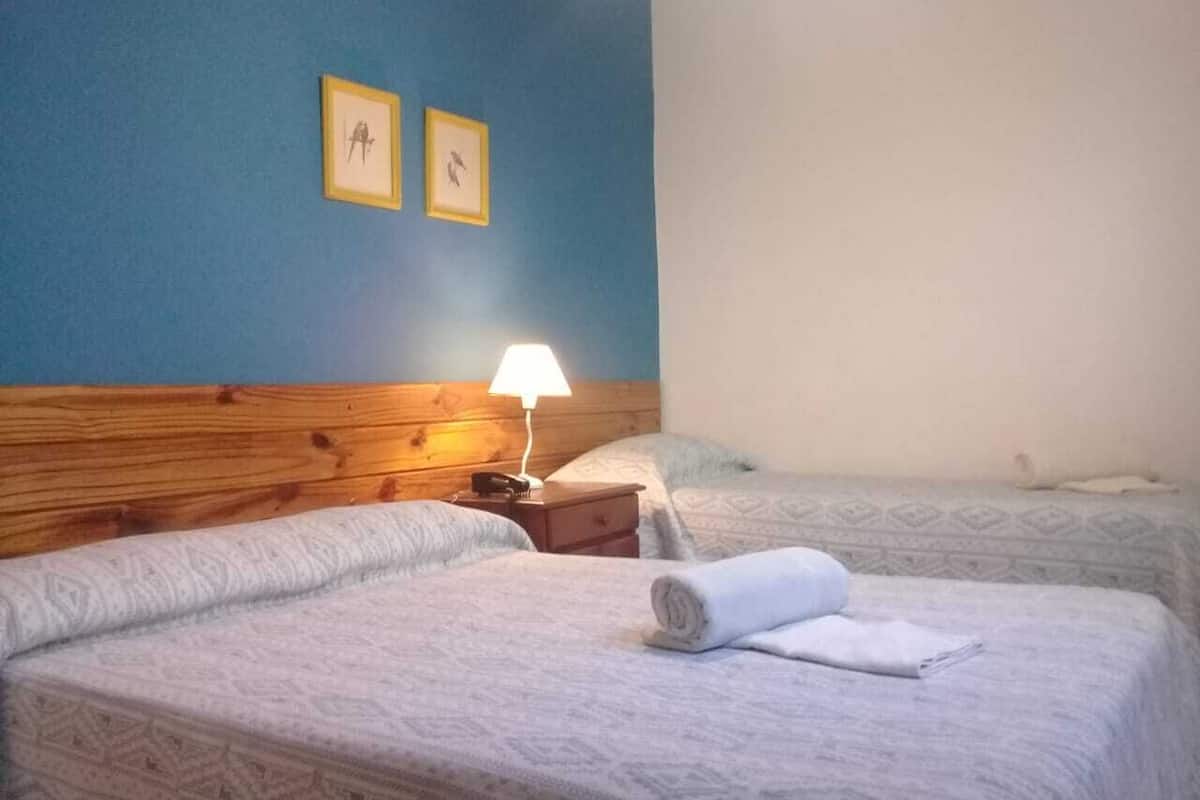 A hotel room with two beds, a wooden headboard, a nightstand with a lamp, and two framed pictures on the wall.