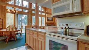 A wooden cabin kitchen with a stove, microwave, and dining area. - Forest Ridge 2 Bedroom Home by RedAwning (Redmond)