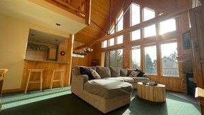 A cozy living room with a large beige sectional sofa, a wooden coffee table, and a fireplace. There are large windows providing natural light and a view of the outside. - Forest Ridge 2 Bedroom Home by RedAwning (Redmond)