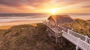 A wooden beach hut with a white railing, overlooking the ocean at sunset. - Point of View - Nags Head MP 15, Oceanfront, Ocean View, Elevator, Pool, Hot Tub, Gazebo (Nags Head)