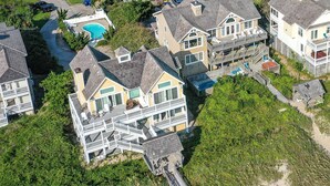 A coastal residential area with multiple two-story houses featuring large balconies and a swimming pool. - Point of View - Nags Head MP 15, Oceanfront, Ocean View, Elevator, Pool, Hot Tub, Gazebo (Nags Head)