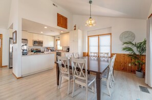 Una cocina moderna con armarios blancos, una isla central y un comedor con mesa y sillas de madera.