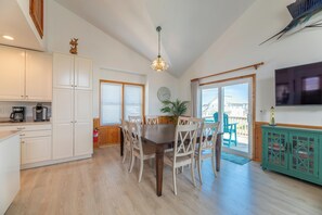 A dining area with a wooden table and chairs, a ceiling light, a television, and a view of the outside.