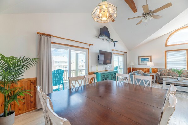 A dining area with a large wooden table, chairs, a ceiling fan, and a mounted fish.