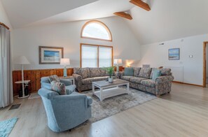 A spacious living room with a high ceiling, a large arched window, and a cozy seating area with a sofa and armchair.