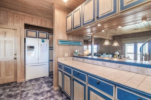 Kitchen area with a refrigerator, countertop, and pendant lights.