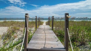 Une promenade en bois menant à la plage, bordée de végétation.