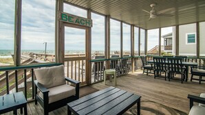 Une terrasse extérieure couverte, aménagée avec des meubles en bois, un panneau indiquant « PLAGE » et une vue sur la plage.