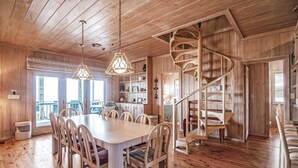 Un intérieur en bois avec un escalier en colimaçon, un coin repas avec des chaises et une table, et une vue par les fenêtres.