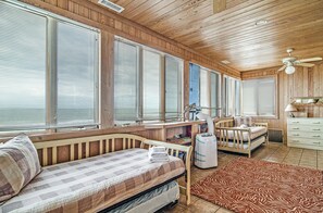 Ein Blockhaus-Interieur mit Holzbalkendecke, großen Fenstern, einem Bett, einem Schreibtisch und einer Küchenzeile.