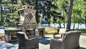 An outdoor seating area with wicker furniture and a stone fireplace. - Lakefront, Historic Estate on the Eagle River Chain of Lakes! Sleeps 42! (Eagle River)