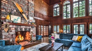 A spacious living room with a fireplace, blue sofas, and large windows. - Lakefront, Historic Estate on the Eagle River Chain of Lakes! Sleeps 42! (Eagle River)