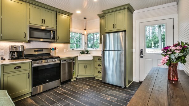 Una cocina moderna con armarios verdes, electrodomésticos de acero inoxidable y suelo de madera.