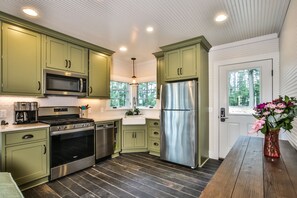Una cocina moderna con armarios verdes, electrodomésticos de acero inoxidable y suelo de madera.