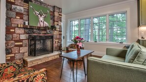 Una sala de estar con chimenea de piedra, un sofá verde, un sillón estampado y una mesa con un jarrón de flores.