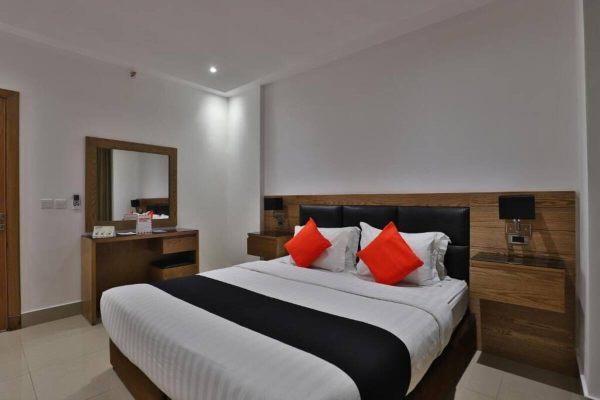A hotel room with a large bed, a wooden headboard, a bedside table with a lamp, and a mirror on the wall.