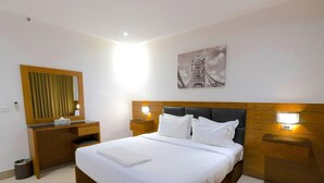 Habitación de hotel ordenada con una cama grande, lámparas de noche, cabecera de madera, un espejo y un cuadro colgado en la pared.