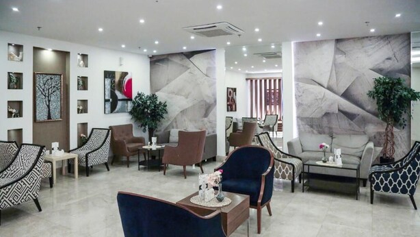 Un moderno vestíbulo de hotel con diversas opciones de asientos, incluyendo sillas y sofás con diseños, una mesa de centro y una pared decorativa con arte abstracto.