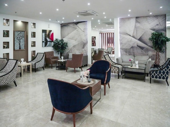 A modern hotel lobby with a mix of seating options, including patterned chairs and sofas, a coffee table, and a decorative wall with abstract art. - Sendan Residence (Dammam)