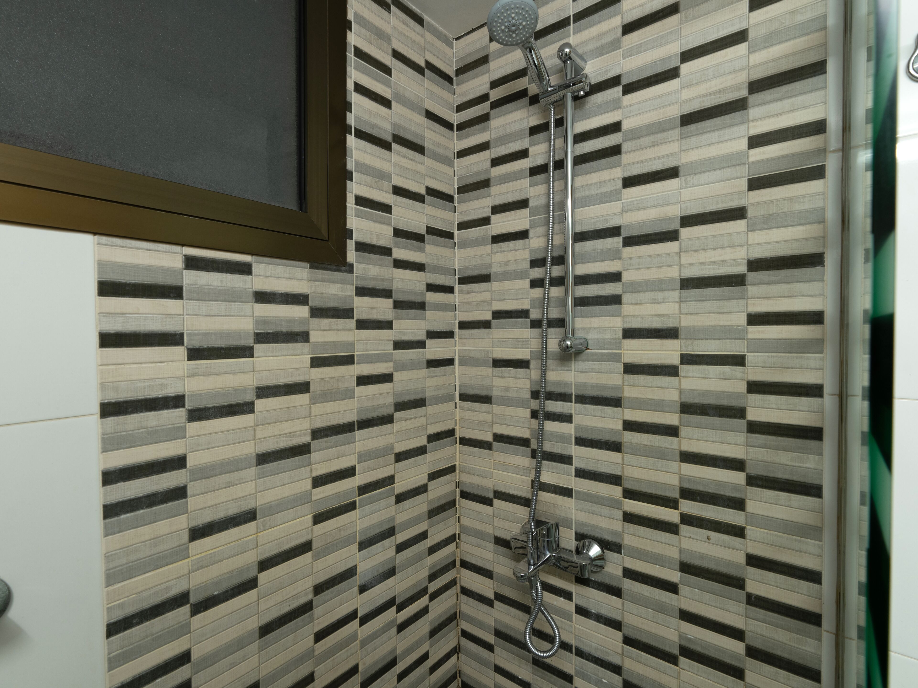 A shower with a handheld showerhead and a wall-mounted faucet.