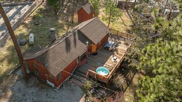 A small cabin with a deck and hot tub, surrounded by trees.