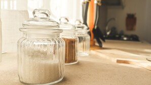 Een aanrecht met glazen potten met suiker en kruiden, een houten lepel en een keukenmes.