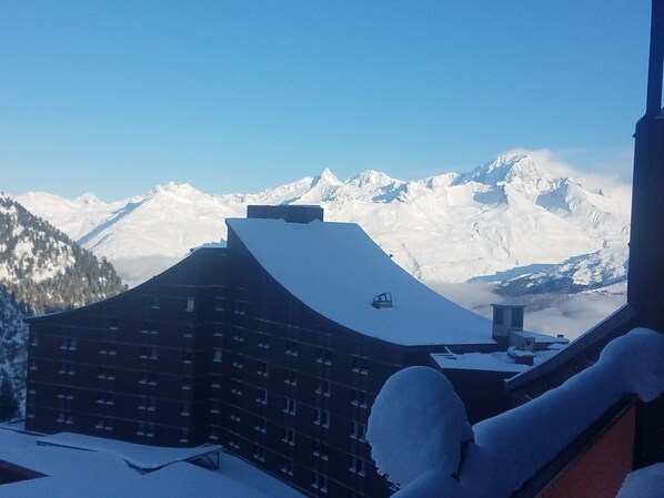 A mountain lodge with a snow-covered roof, a ski lift, and snow-covered mountains in the background.