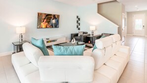 A modern living room with a white sofa, a coffee table, and a TV mounted on the wall. - Colorful Villa with Theater at Encore (Kissimmee)