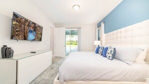 A bedroom with a bed, a dresser, a TV mounted on the wall, and a door leading to a balcony. - Colorful Villa with Theater at Encore (Kissimmee)